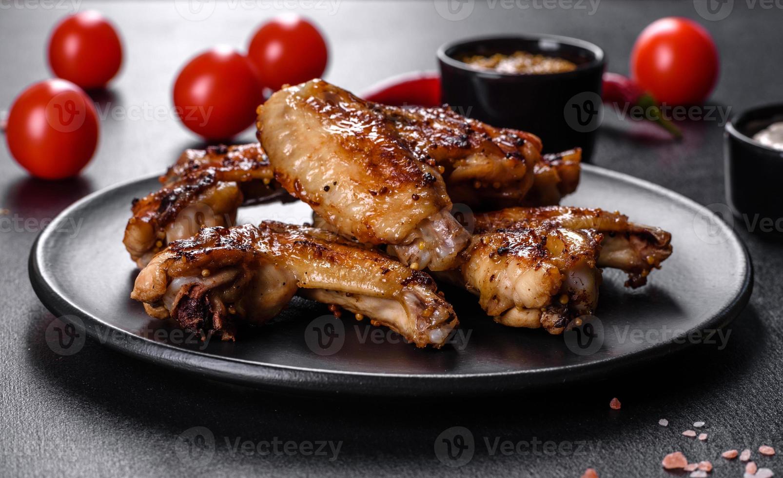 gegrillte würzige Hähnchenflügel auf dunklem Hintergrund mit Gewürzen und Kräutern foto