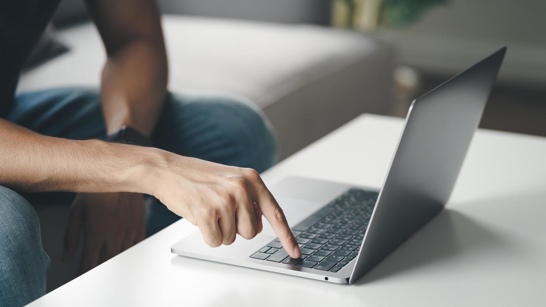 Mann sitzt zu Hause auf dem Sofa und tippt auf der Laptop-Tastatur foto