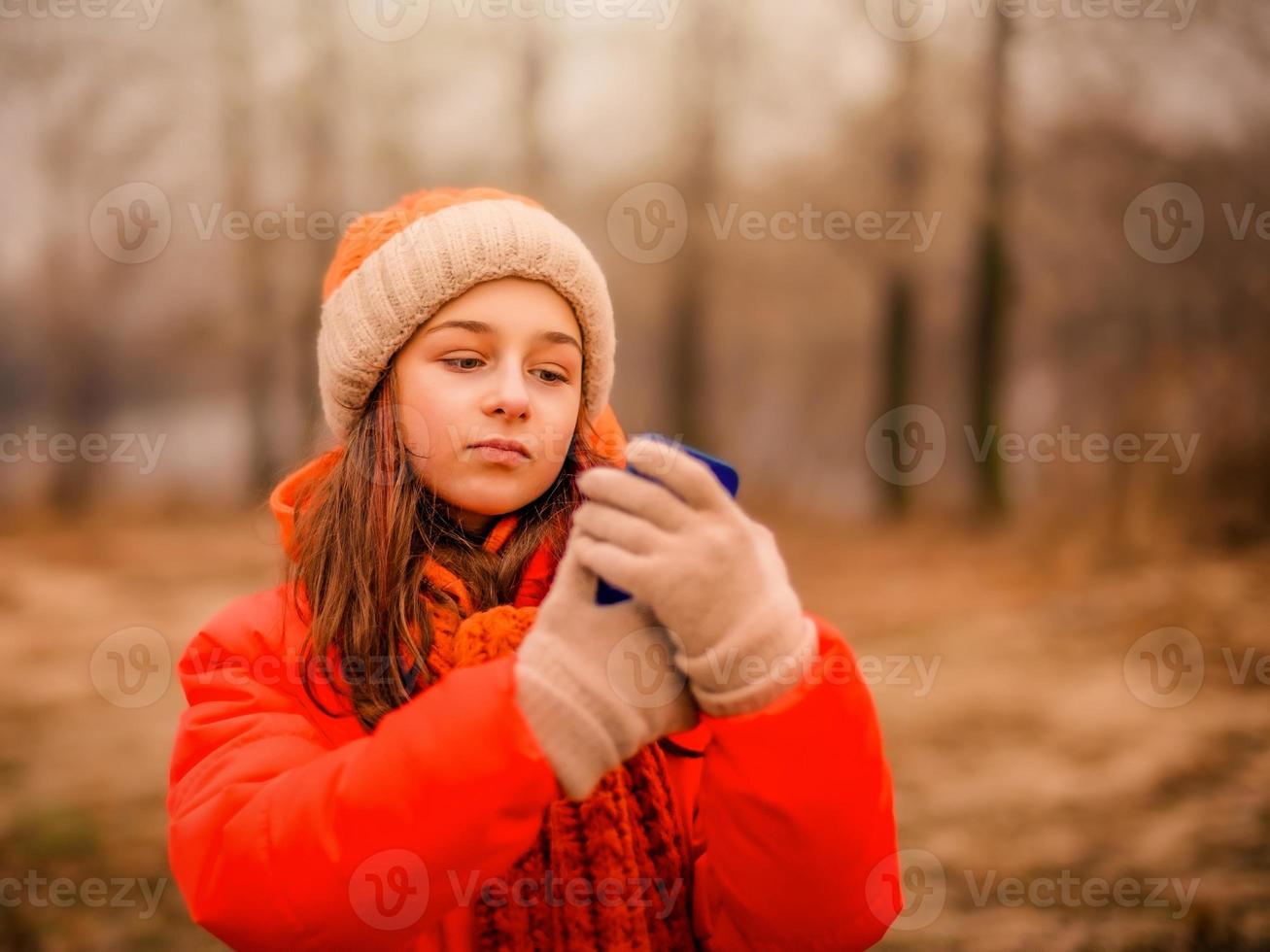 Teenager-Mädchen schaut im Herbst oder Winter im Park in ein Smartphone. foto