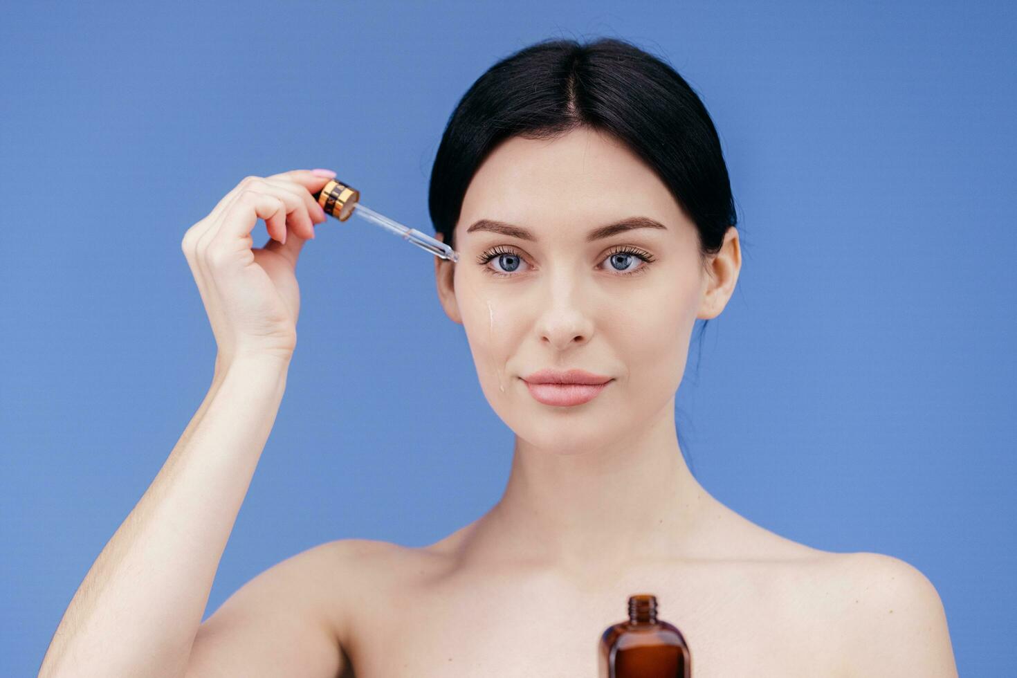 europäisch jung Frau gilt Gesicht Pflege Serum auf ihr Wange von Tropfer auf Weiß Hintergrund. Gesicht Pflege Serum Werbung foto