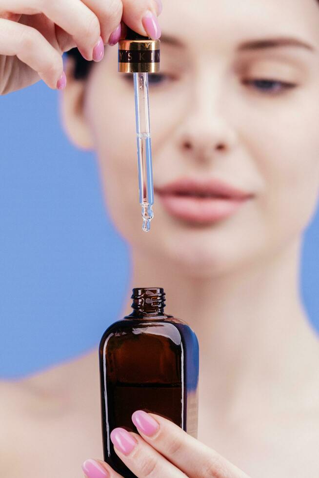 europäisch jung Frau gilt Gesicht Pflege Serum auf ihr Wange von Tropfer auf Weiß Hintergrund. Gesicht Pflege Serum Werbung foto