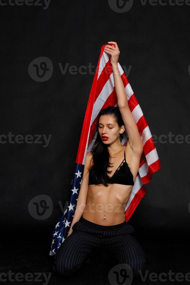 Porträt weiblich Athlet eingewickelt im amerikanisch Flagge gegen schwarz Hintergrund foto