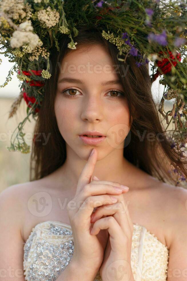 schön Frau mit ein Kranz auf ihr Kopf Sitzung im ein Feld im Blumen foto