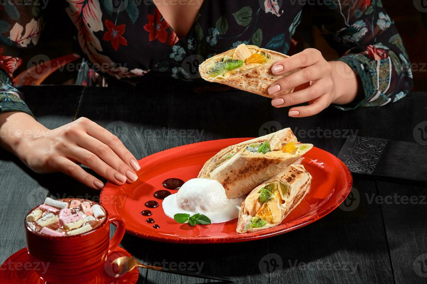 weiblich Hände halten Obst rollen im dünn Lavash serviert mit Eis Sahne und Tasse von Kakao foto