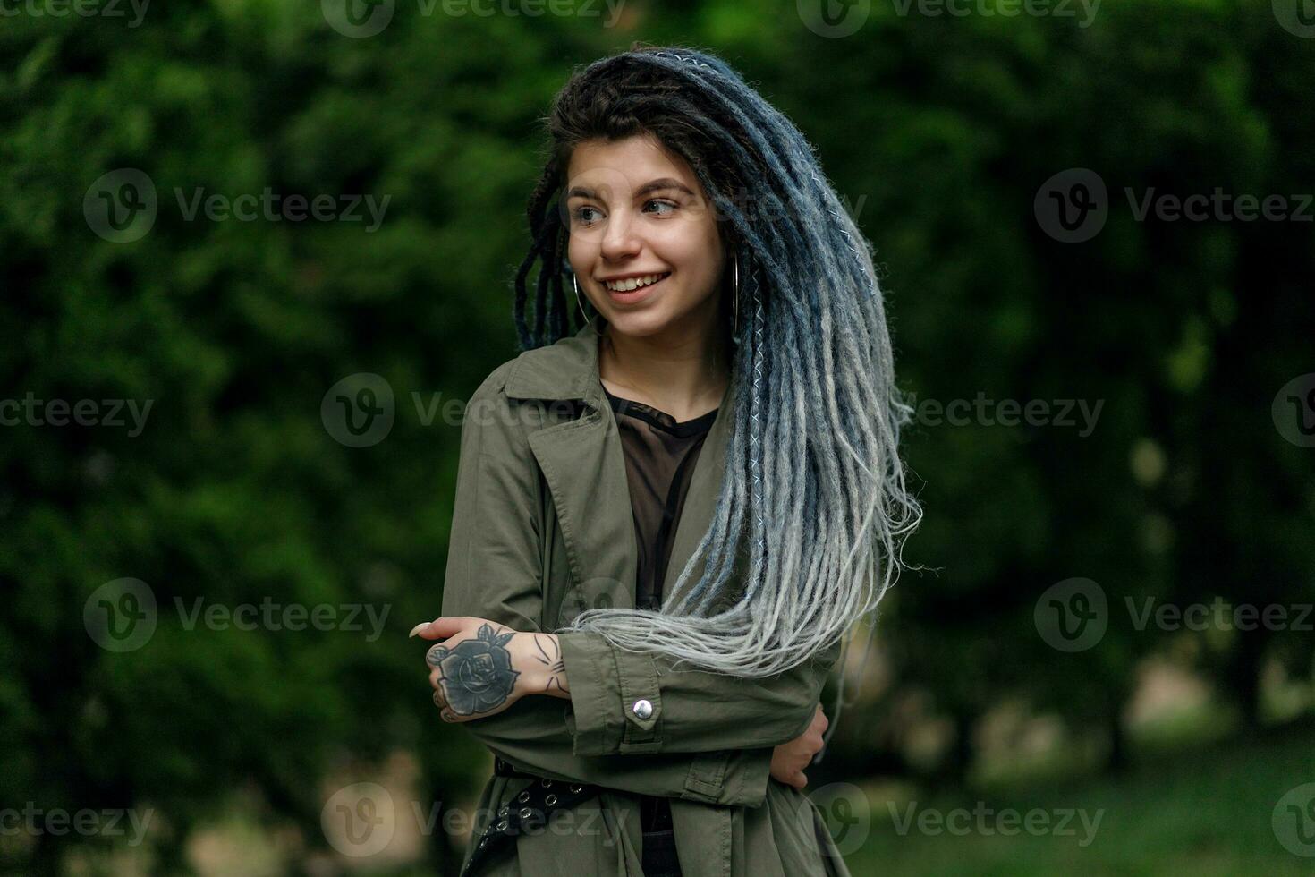 heiter kaukasisch Mädchen suchen beim das Kamera und lächelnd Modell- mit Dreadlocks foto