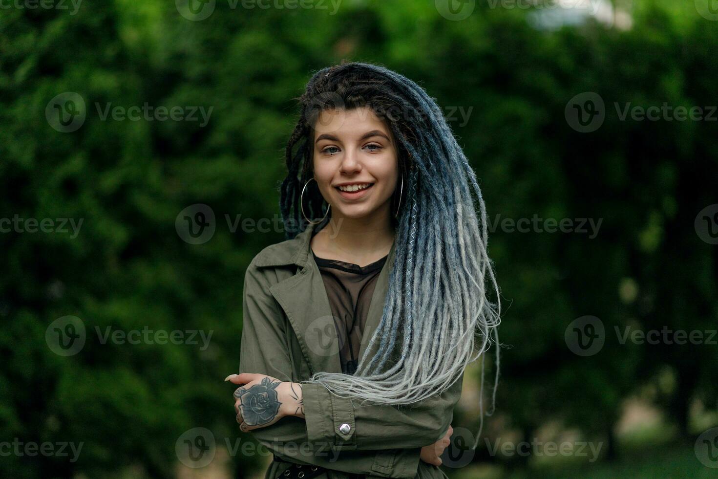 heiter kaukasisch Mädchen suchen beim das Kamera und lächelnd Modell- mit Dreadlocks foto