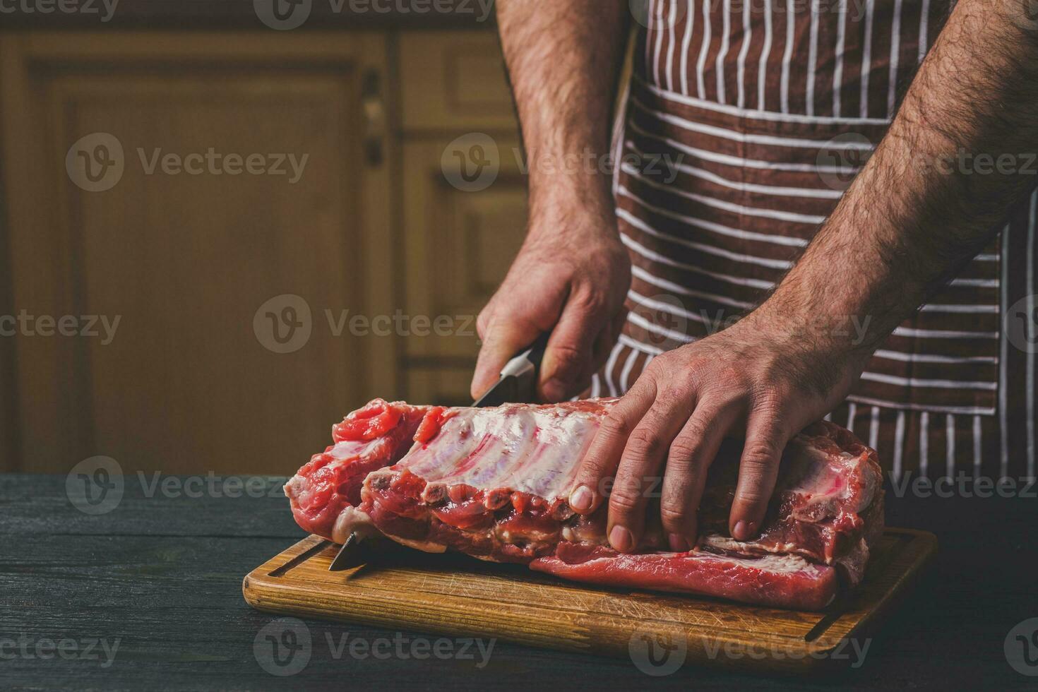 Mann schneidet von frisch Stück von Fleisch auf ein hölzern Schneiden Tafel im das Zuhause Küche foto