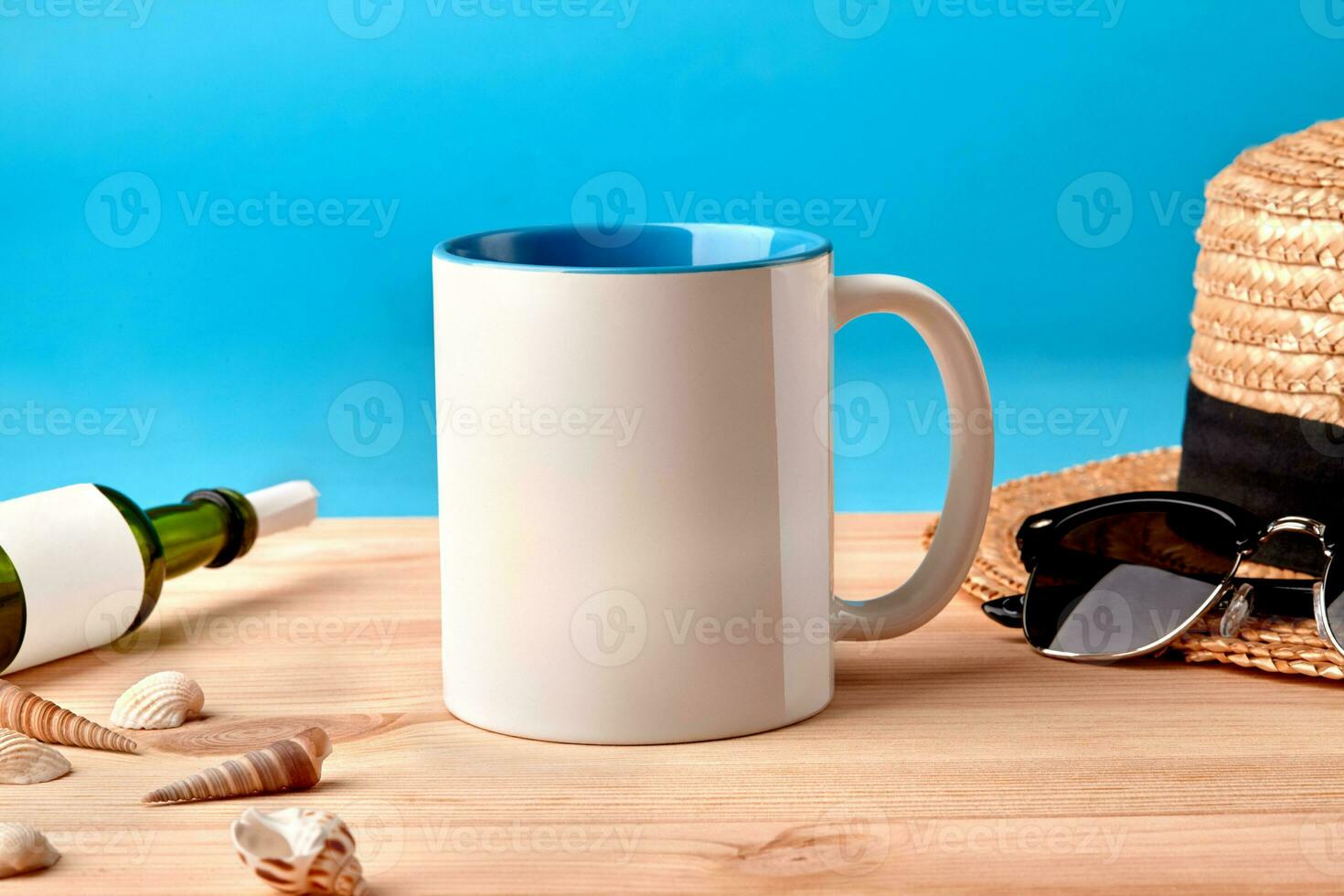 Weiß Keramik Becher auf hölzern Desktop Nächster zu Muscheln, Flasche mit gerollt Blatt von Papier im Es, Stroh Hut und schwarz Sonnenbrille, Blau Hintergrund foto