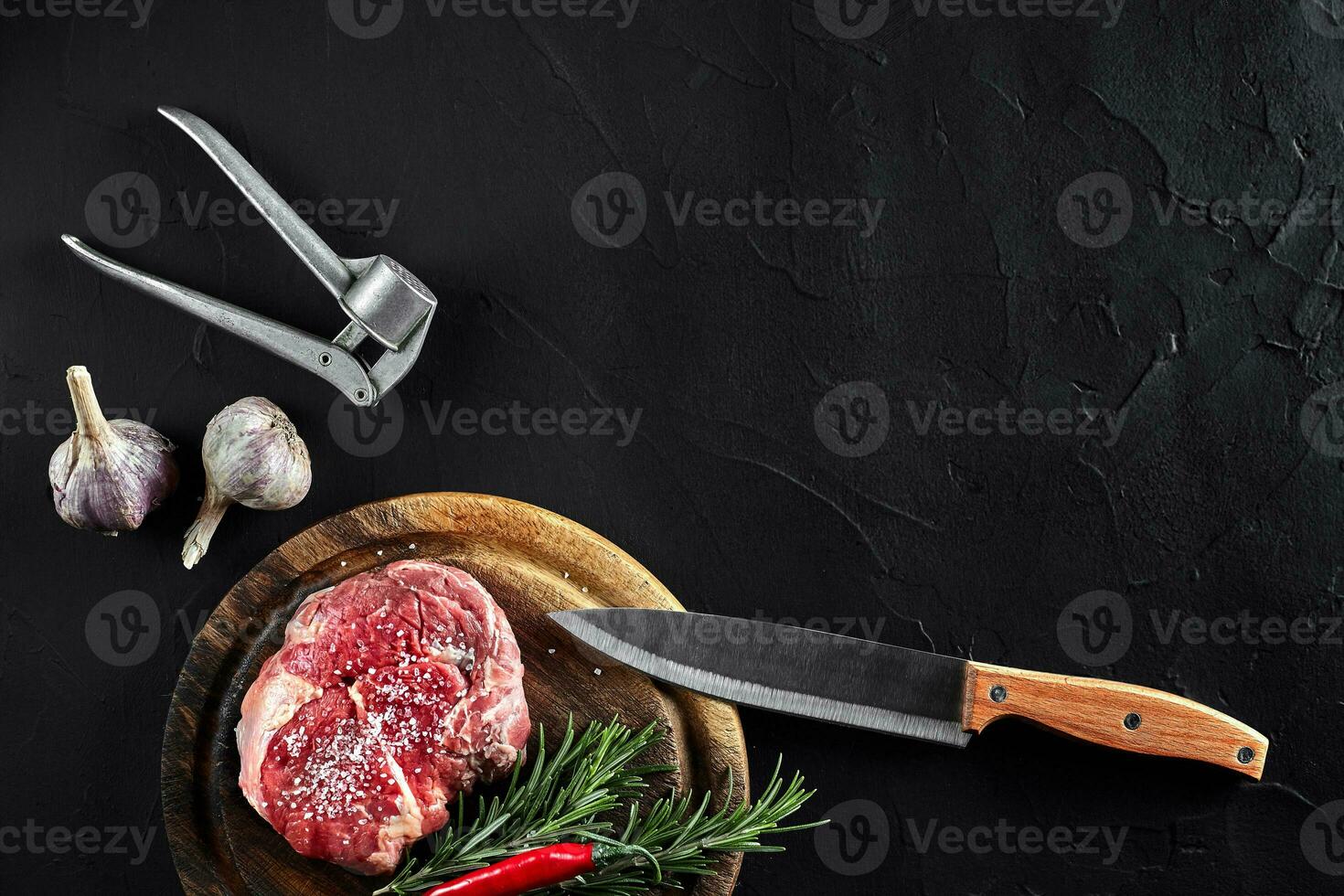 Stück von Rindfleisch Filet, mit Messer zum Schneiden und Hacken Fleisch, Gewürze wurden Kochen - - Rosmarin, Pfeffer, Salz, Knoblauch. auf alt hölzern Tafel auf Stein schwarz Tisch. foto