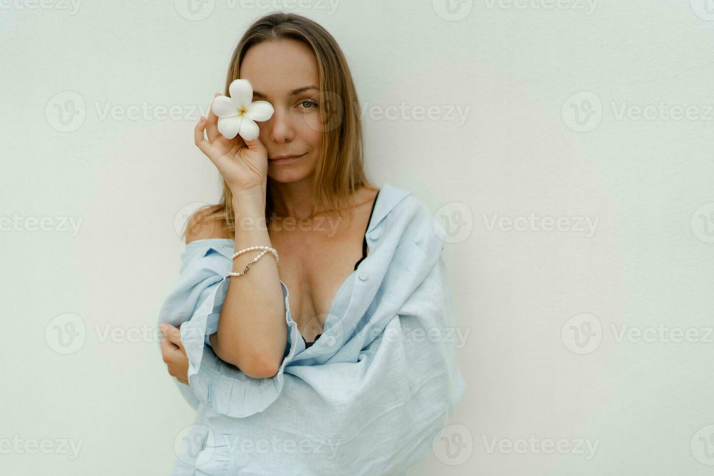 stilvoll Brünette Frau im schön Blau Spielanzug halten Blume und posieren Über Weiß Mauer. foto