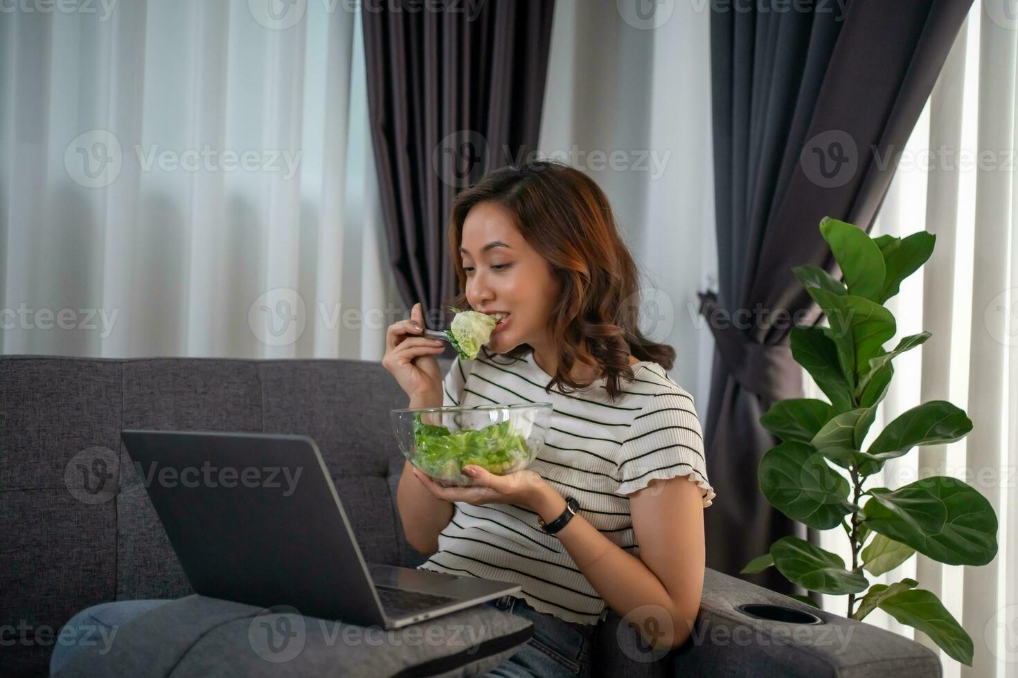 Frau Essen gesund Salat zum Mittagessen während Arbeiten mit Laptop beim Zuhause Büro. foto