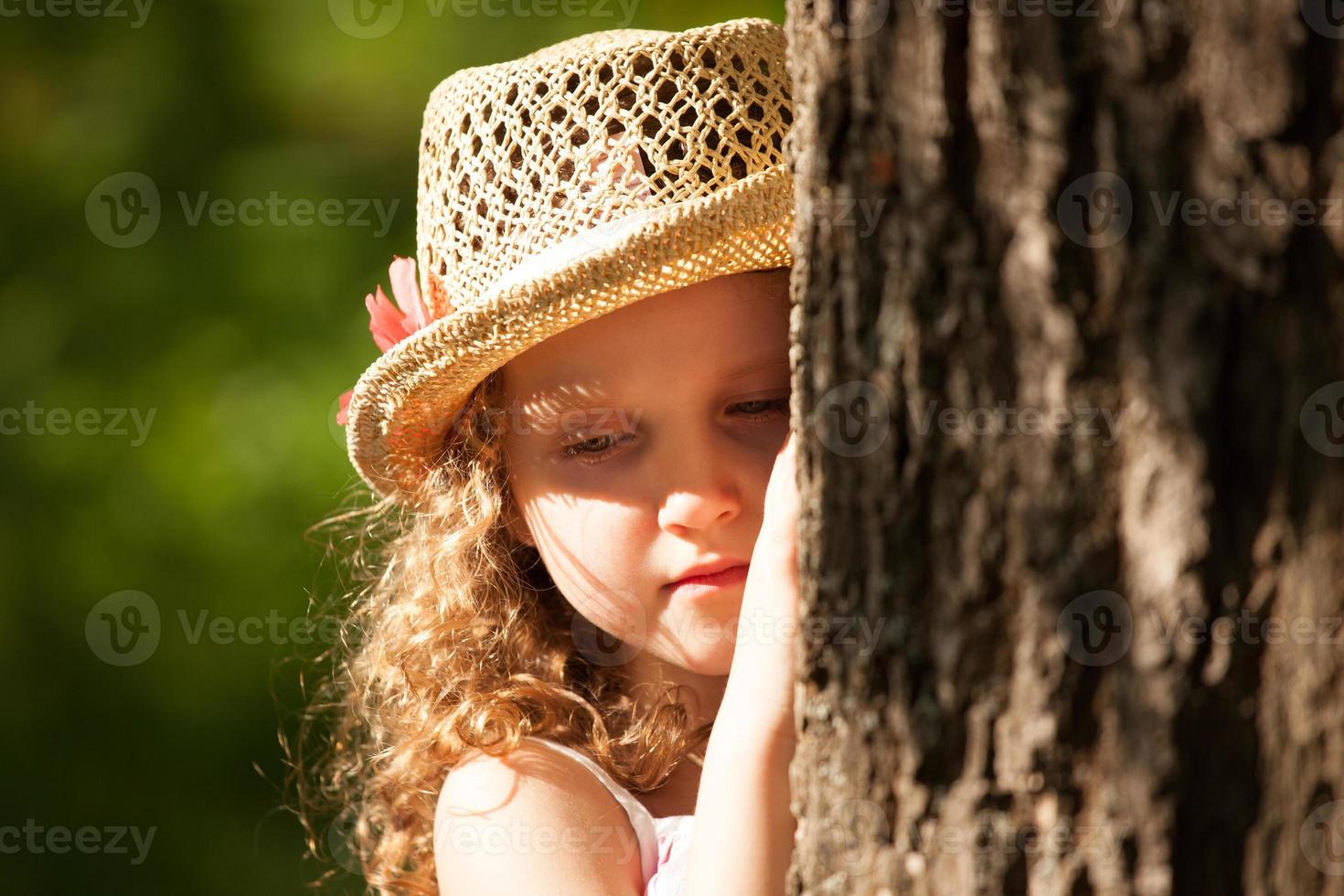 Mädchen mit Hut, das in Gedanken neben dem Baum steht foto