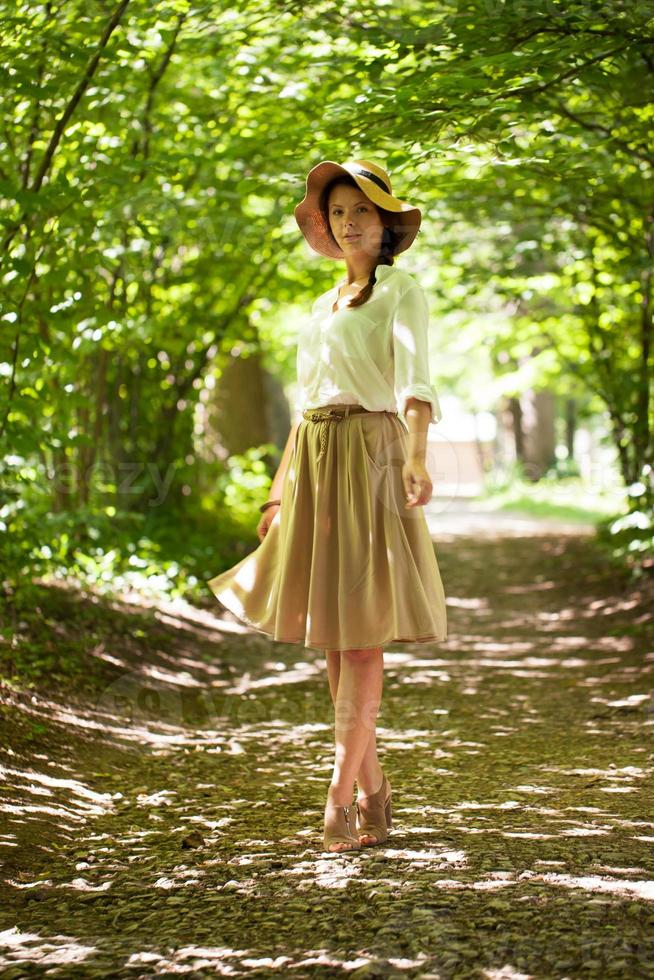 schöne elegante Frau mit Hut unter grünem Laub foto