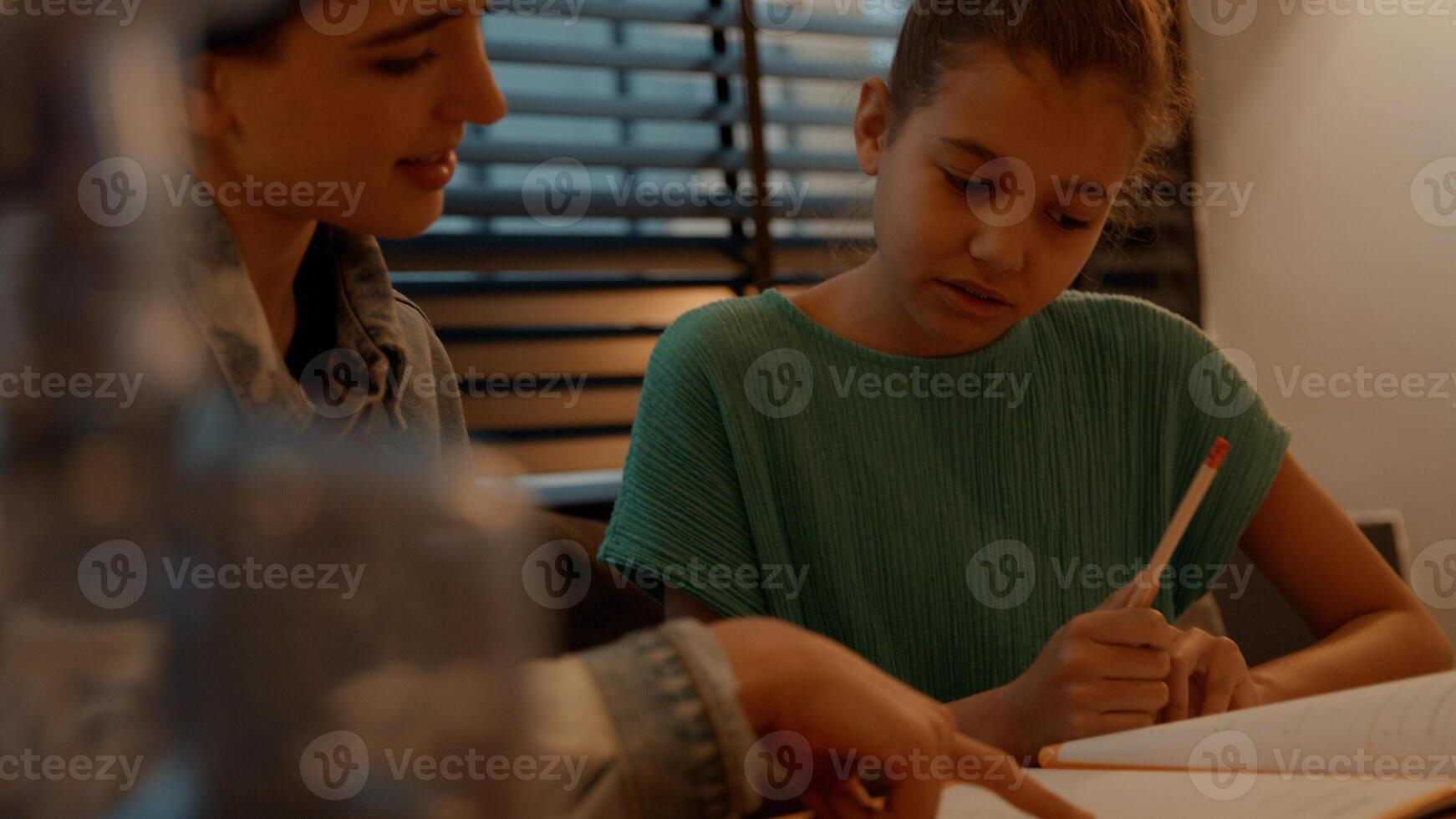 Frau, die Mädchen hilft, Hausaufgaben am Tisch zu machen foto