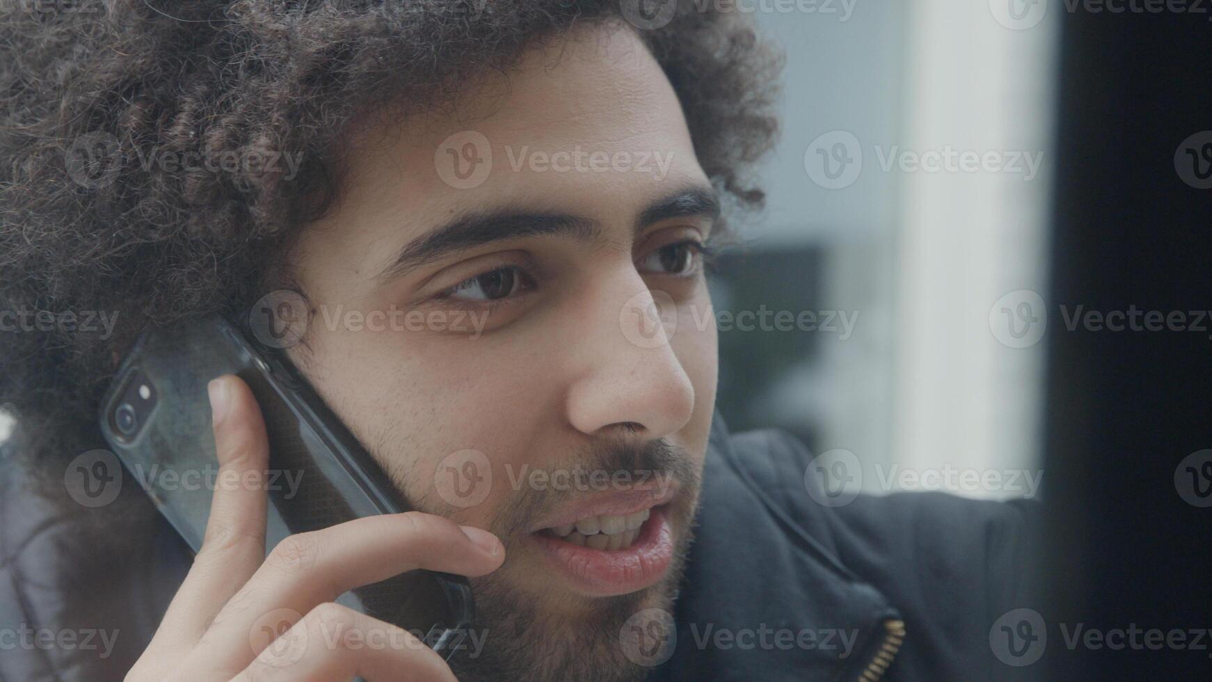 junger Mann aus dem Nahen Osten spricht lebhaft und hält Handy am Ohr foto