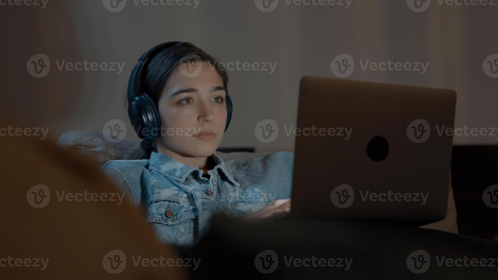 Frau auf der Couch mit Kopfhörer, der Laptop beobachtet foto