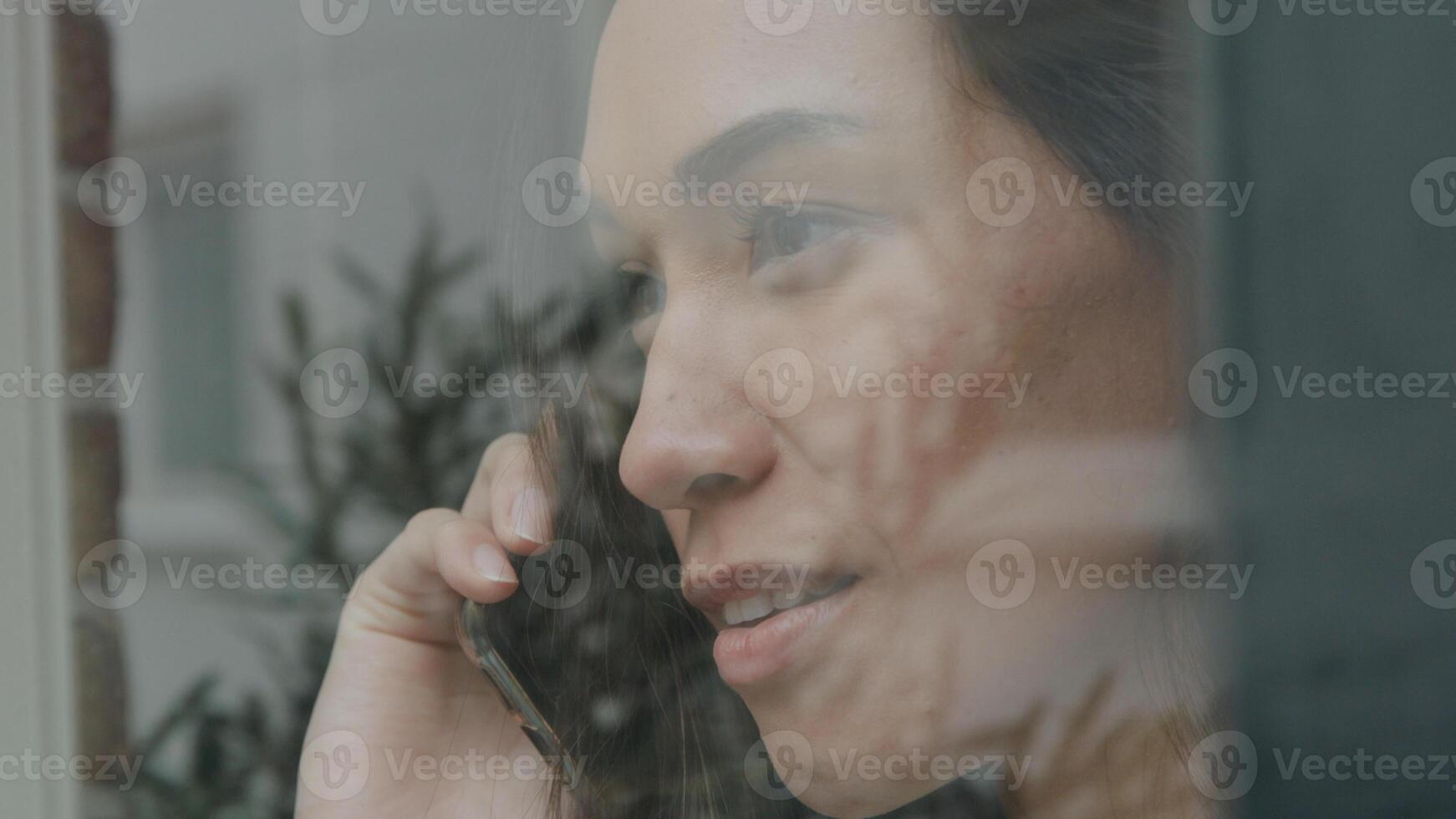 junge gemischtrassige Frau, die anruft, während sie durch das Fenster schaut foto