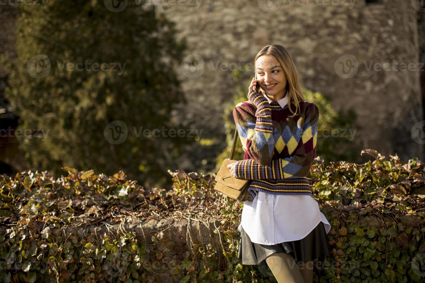 hübsche junge frau, die am herbsttag mit handy auf der straße steht foto