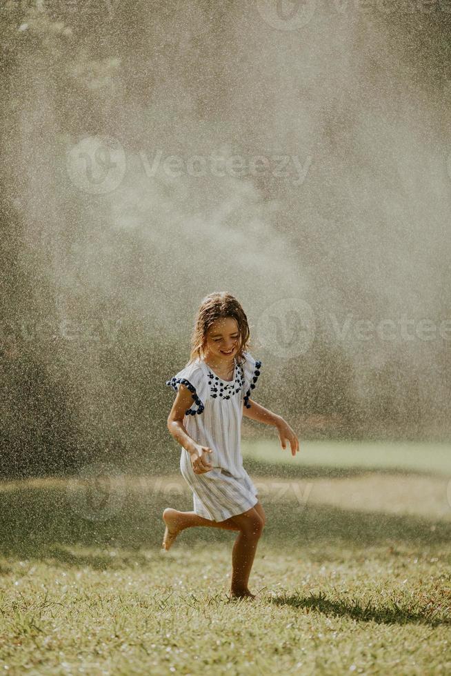 süßes kleines Mädchen, das Spaß unter Bewässerungssprinkler hat foto