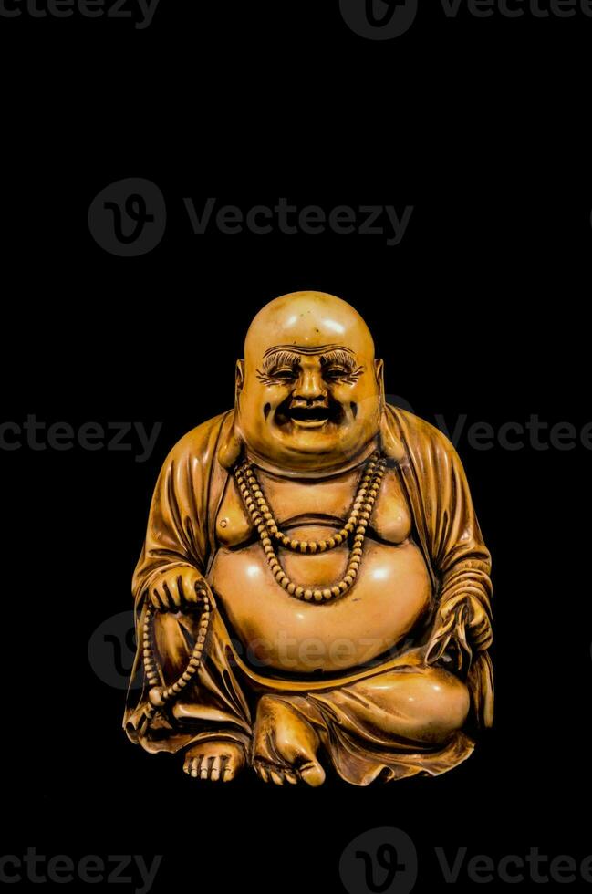ein Statue von ein lächelnd Buddha Sitzung auf ein schwarz Hintergrund foto