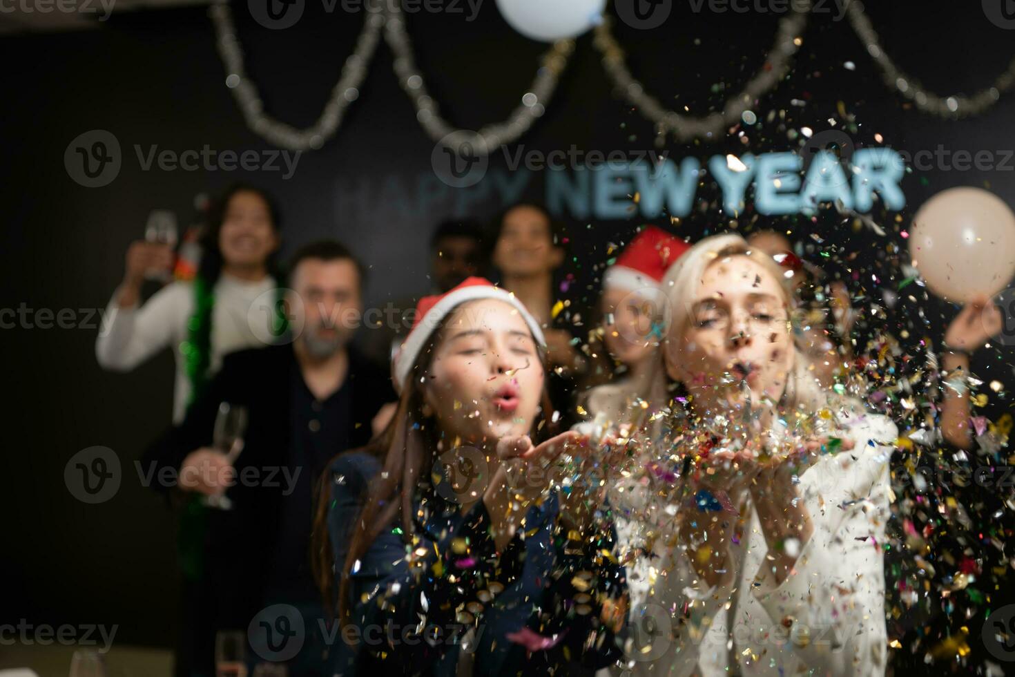 Neu Jahr Party, Gruppe von jung Menschen im Santa Hüte weht Konfetti während feiern Neu Jahr foto