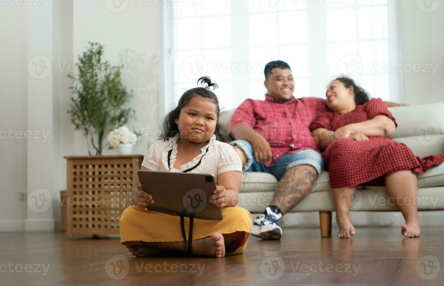 ein Plus Größe Familie mit ein Vater tragen ein Prothese Bein, während sich ausruhen Zeit ermöglichen Tochter zu abspielen Spiele auf Tablette im das Leben Zimmer von das Haus. foto