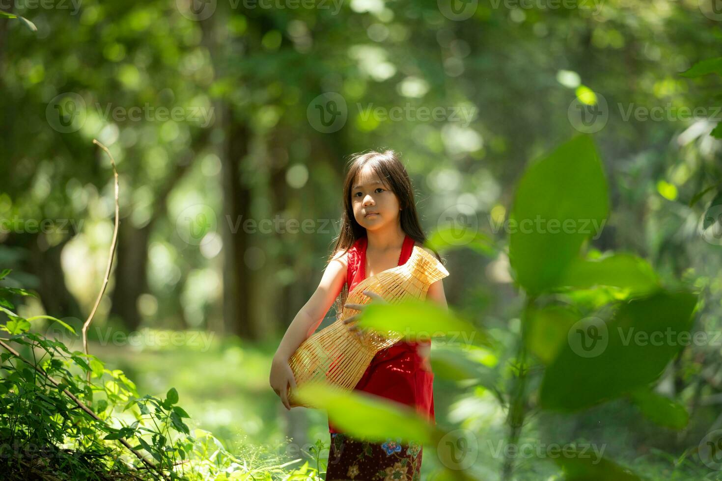 wenig asiatisch Mädchen im rot Kleid halten Angeln Ausrüstung im das Wald, ländlich Thailand Leben Leben Konzept foto