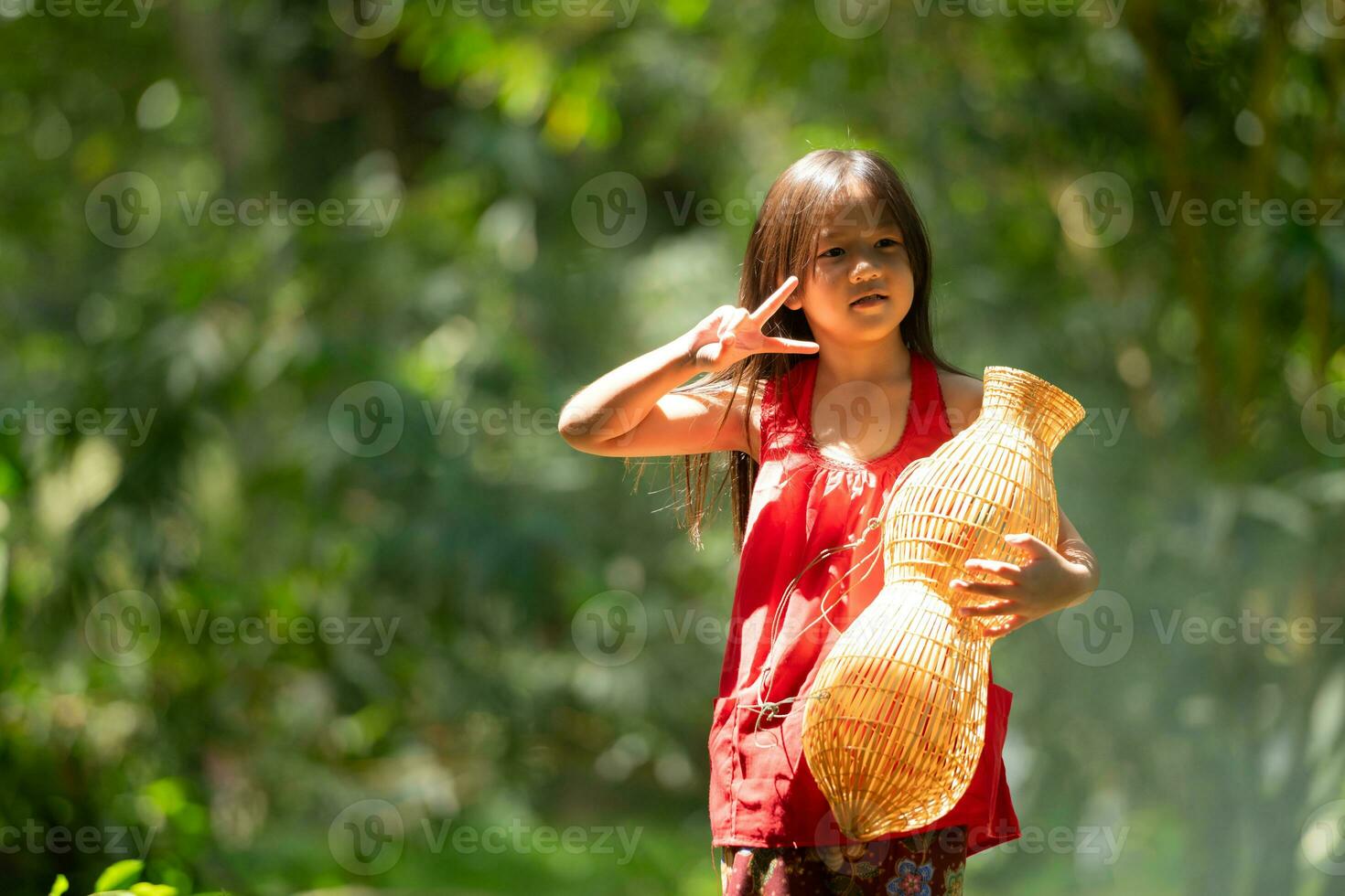 wenig asiatisch Mädchen im rot Kleid halten Angeln Ausrüstung im das Wald, ländlich Thailand Leben Leben Konzept foto