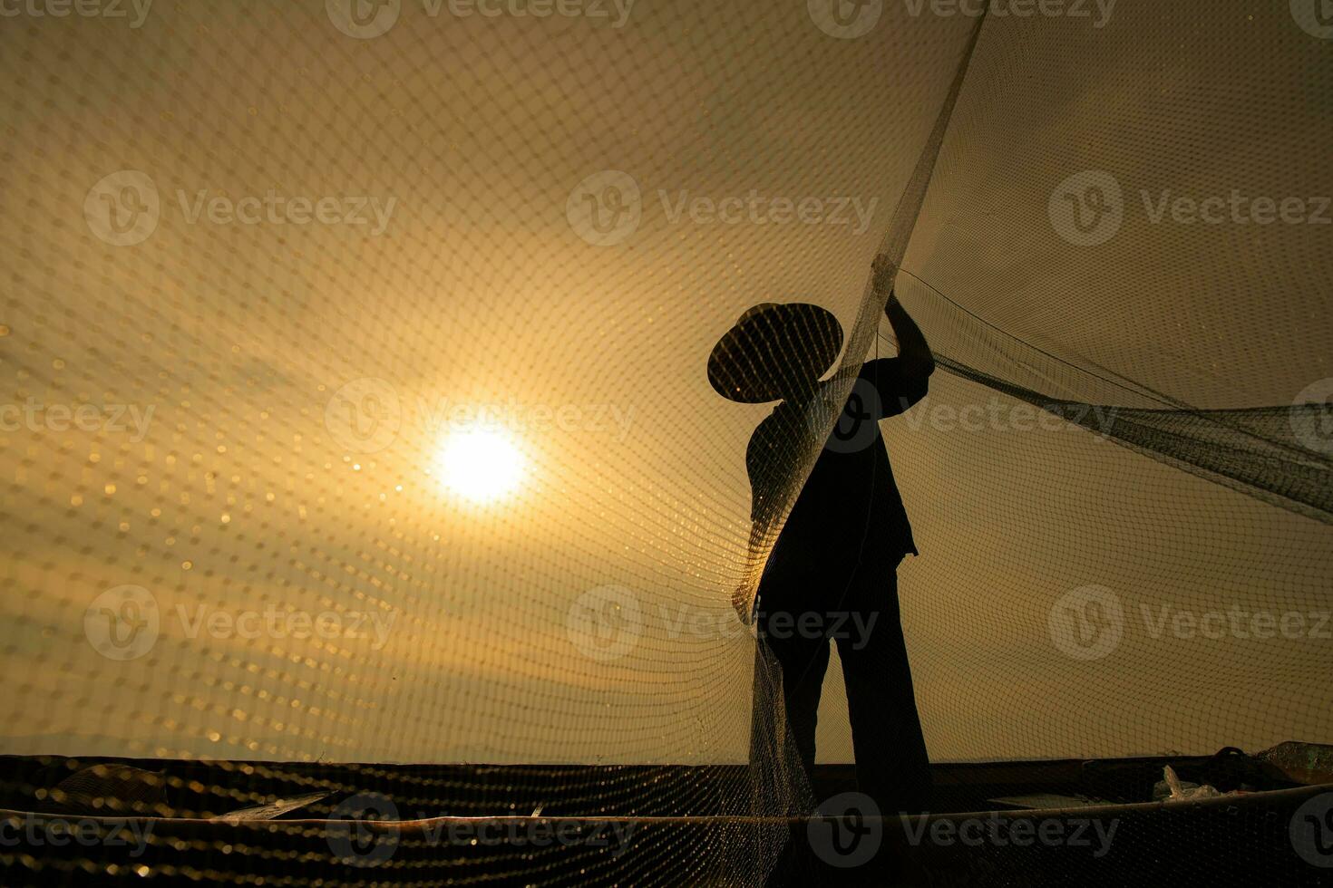 Silhouette von Fischer beim Sonnenaufgang, Stehen an Bord ein Rudern Boot und Gießen ein Netz zu Fang Fisch zum Essen foto