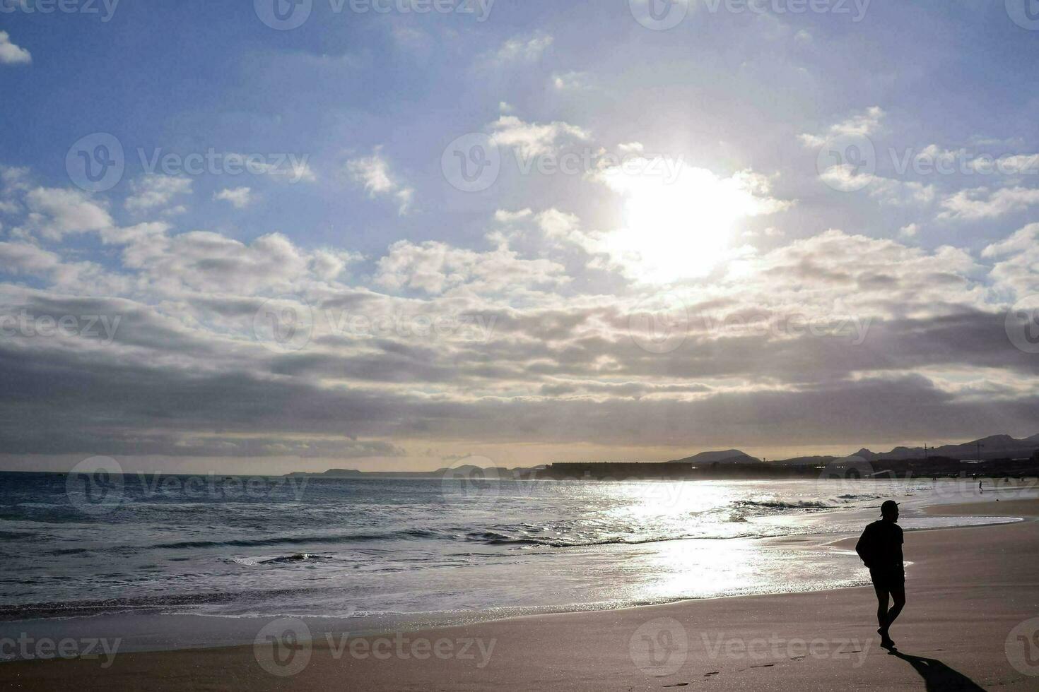 ein Person Gehen auf das Strand im Vorderseite von das Sonne foto
