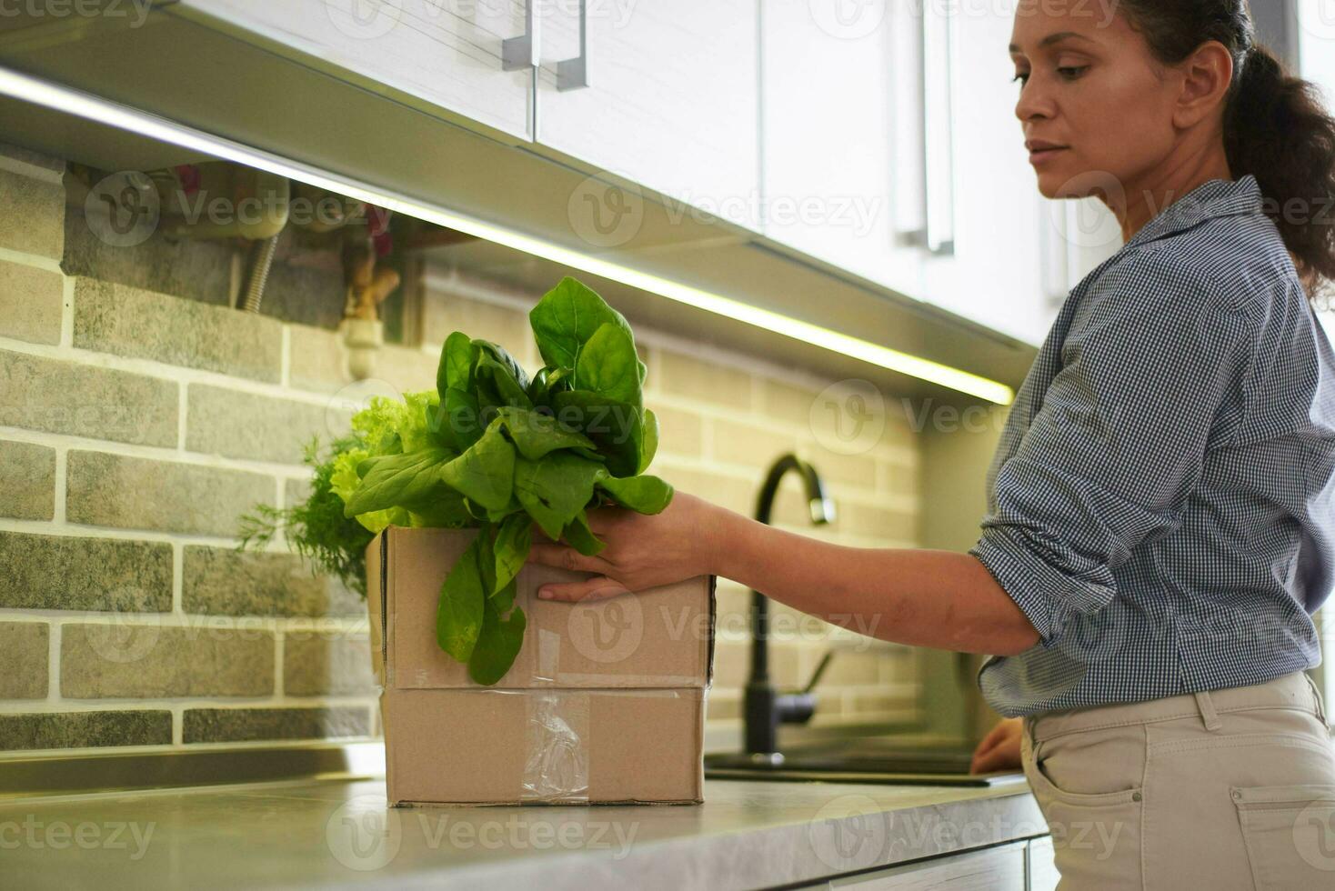 schön Hausfrau Stehen durch Küche Zähler und Sortierung frisch Salat Blätter und Grüns im ein Karton Box foto