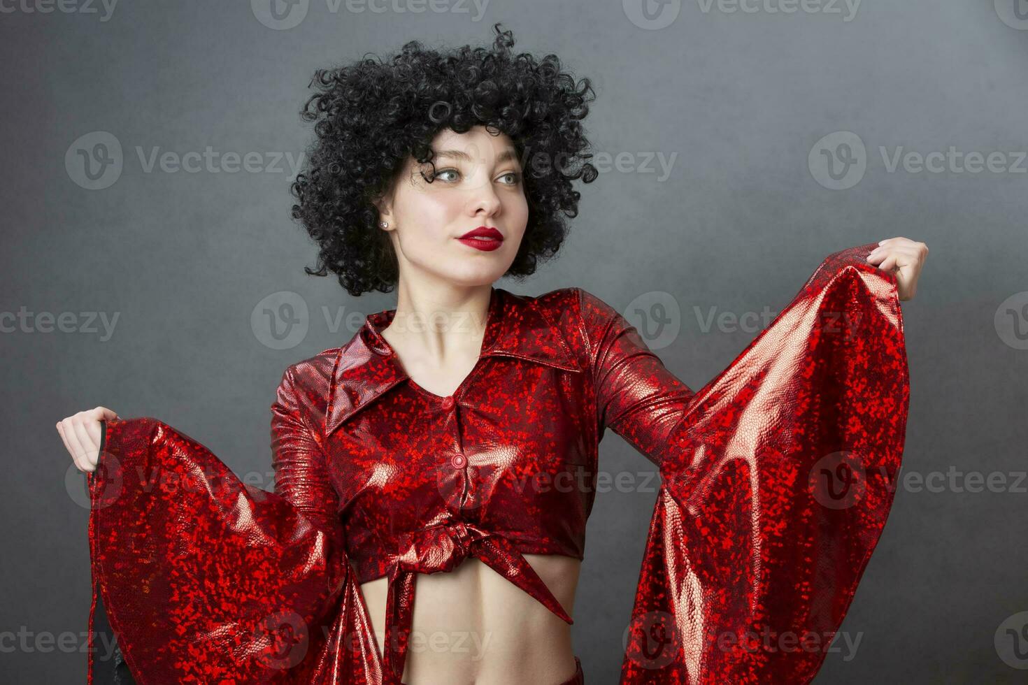 Jahrgang Frau im afro Perücke und rot Disko Kostüm auf ein grau Hintergrund. Mädchen im das Stil von das siebziger Jahre. foto