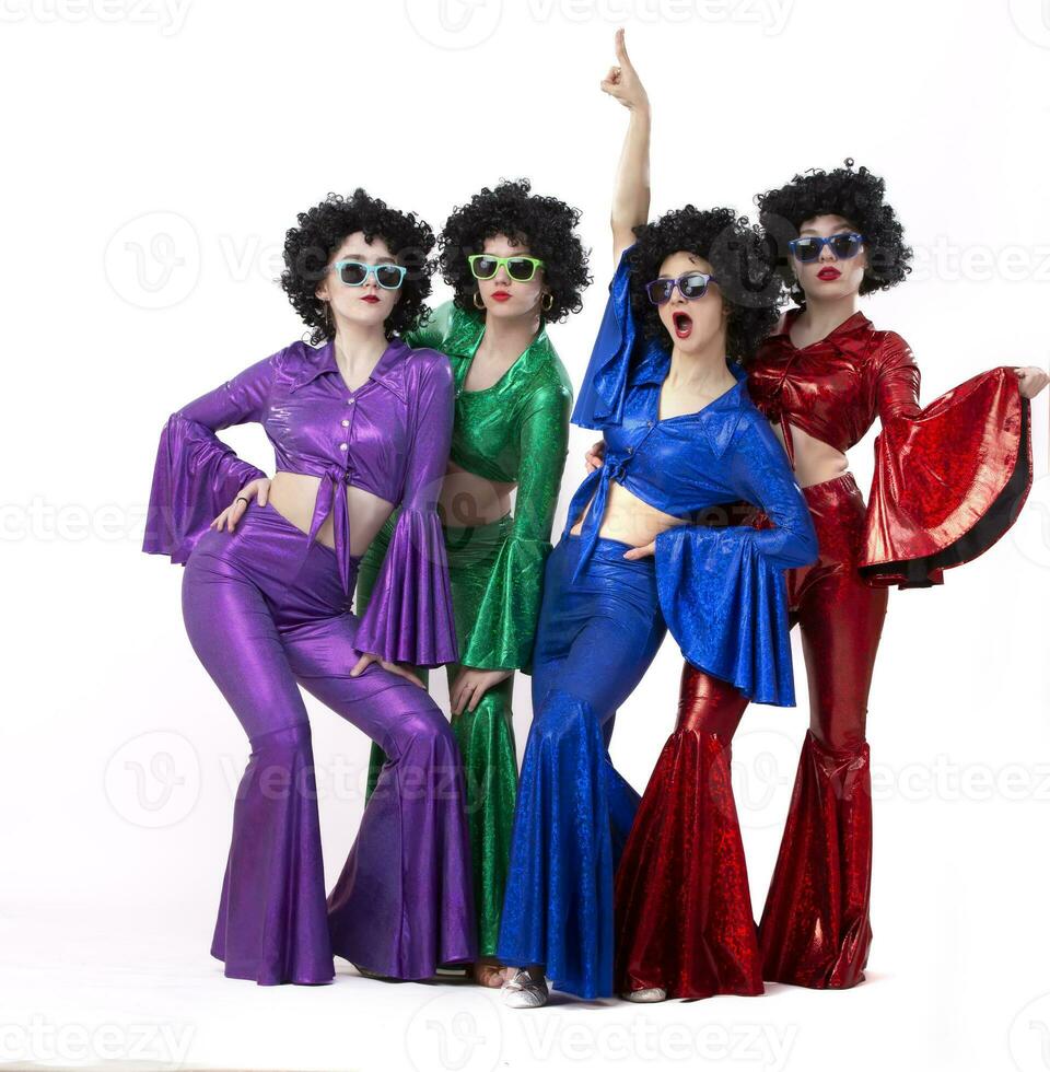 ein Gruppe von Mädchen im bunt aufgeflammt Anzüge und afro Perücken Pose gegen ein Weiß Hintergrund. Disko Stil von das achtziger Jahre oder siebziger Jahre. foto