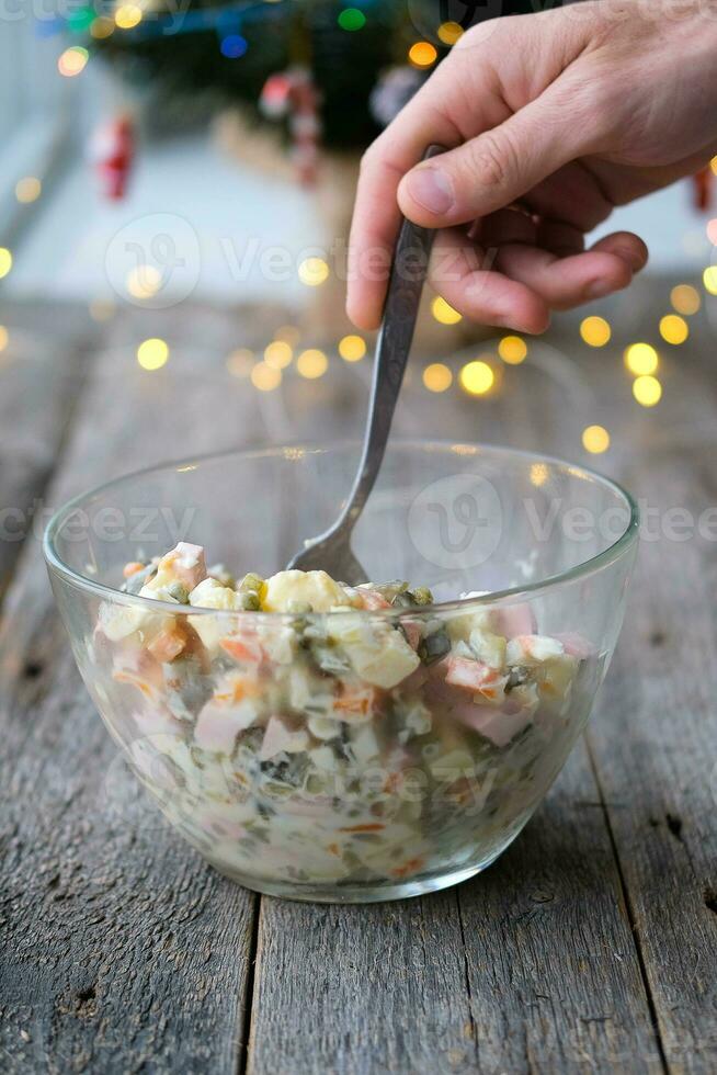 hausgemacht Neu Jahr ist Olivier Salat auf ein hölzern Hintergrund. ein des Mannes Hand setzt ein traditionell Russisch Weihnachten Salat mit ein Löffel. foto