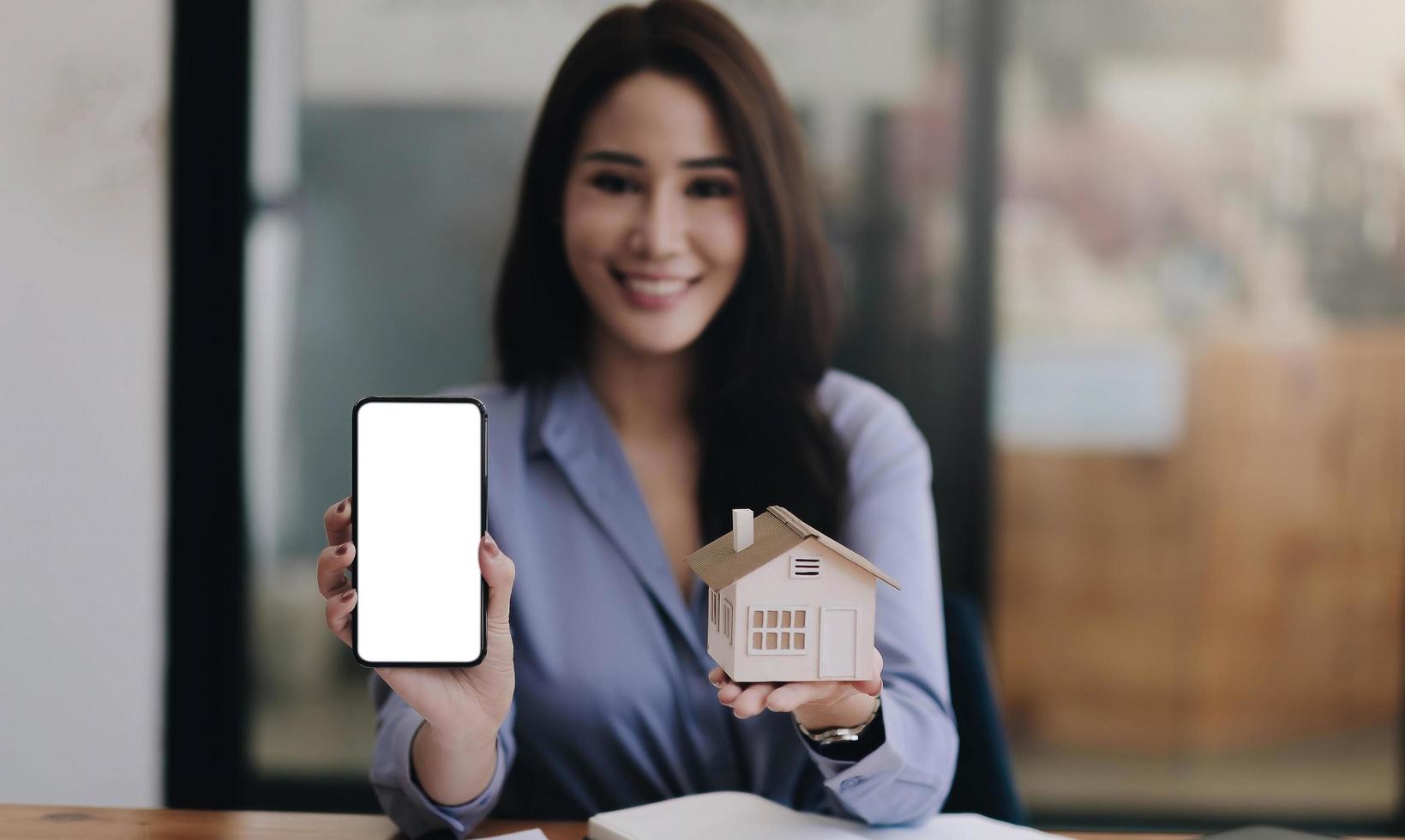 Immobilienmakler, der Hausmodell mit leerem weißem Bildschirm zeigt foto