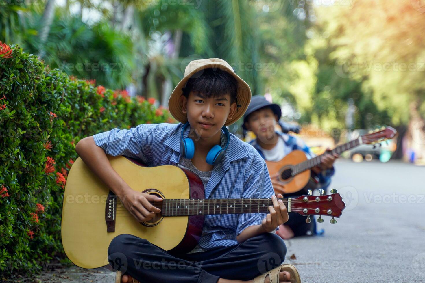 zwei asiatisch Jungs wurden haben Spaß spielen klassisch Gitarre zusammen während ihr kostenlos Zeit beim ein Schule Sommer- Lager beim das Park. Sanft und selektiv Fokus. foto