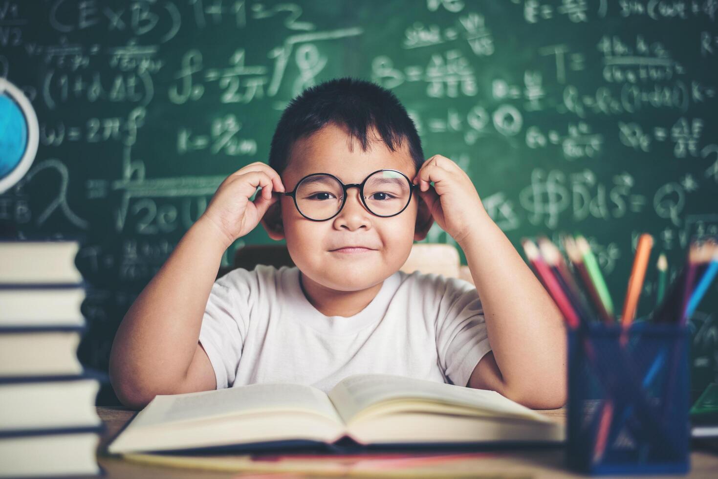 nachdenklicher kleiner Junge mit Buch im Klassenzimmer foto