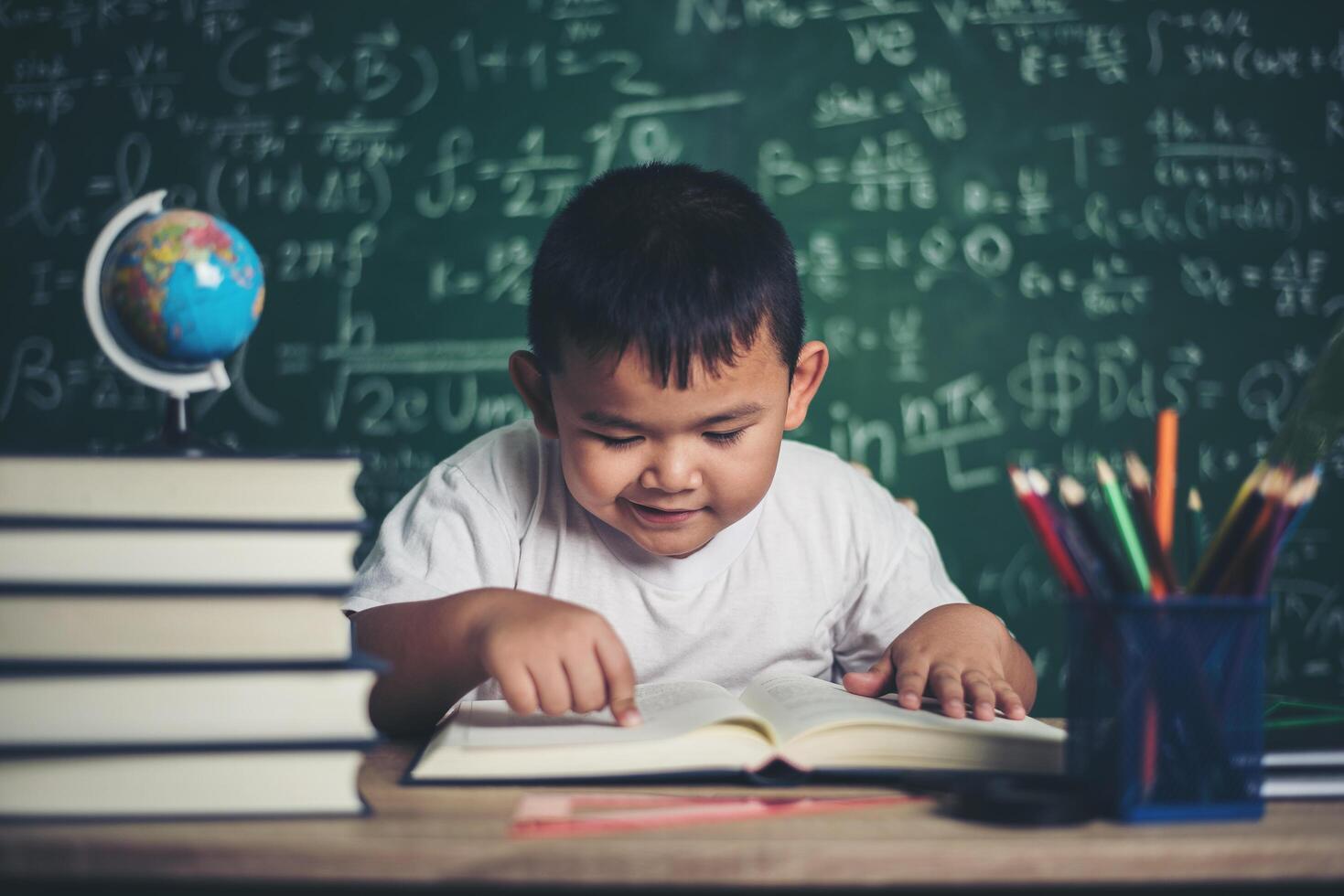 Junge liest ein Buch am Tisch im Klassenzimmer sitzen foto