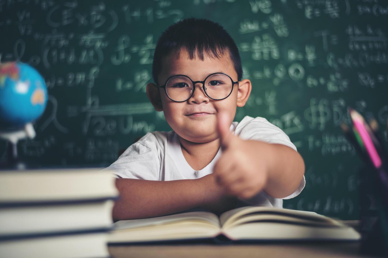 Porträt eines Jungen mit den Händen Daumen hoch im Klassenzimmer. foto