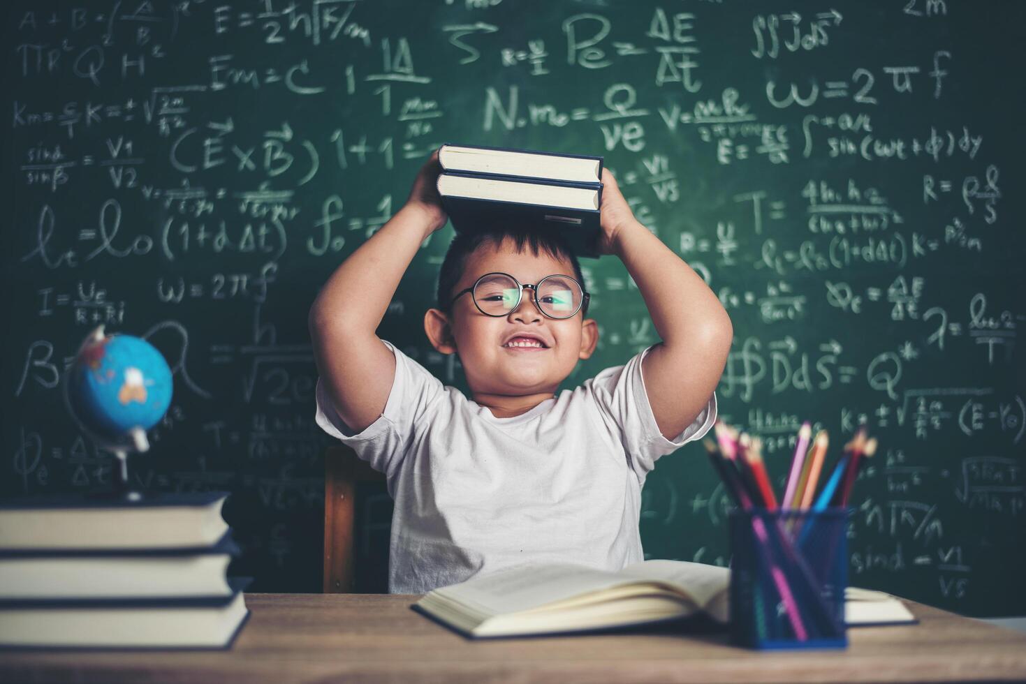 Junge mit Büchern, die im Klassenzimmer sitzen foto