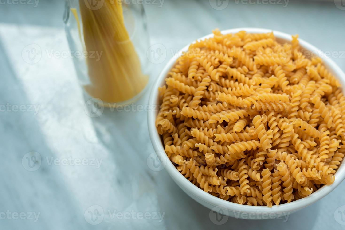 Blick von oben auf die weiße Schüssel mit Spiralmakkaroni und gebundenen Spaghetti foto