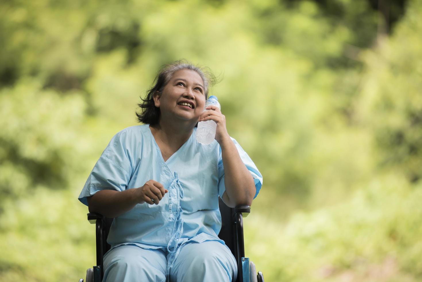 Alte Frau sitzt mit Wasserflasche im Rollstuhl, nachdem sie ein Medikament eingenommen hat foto