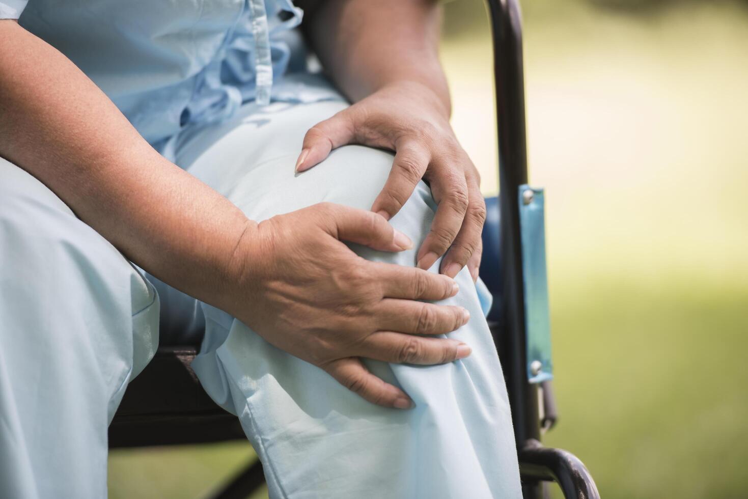 ältere Frau, die mit Knieschmerzen im Rollstuhl sitzt foto