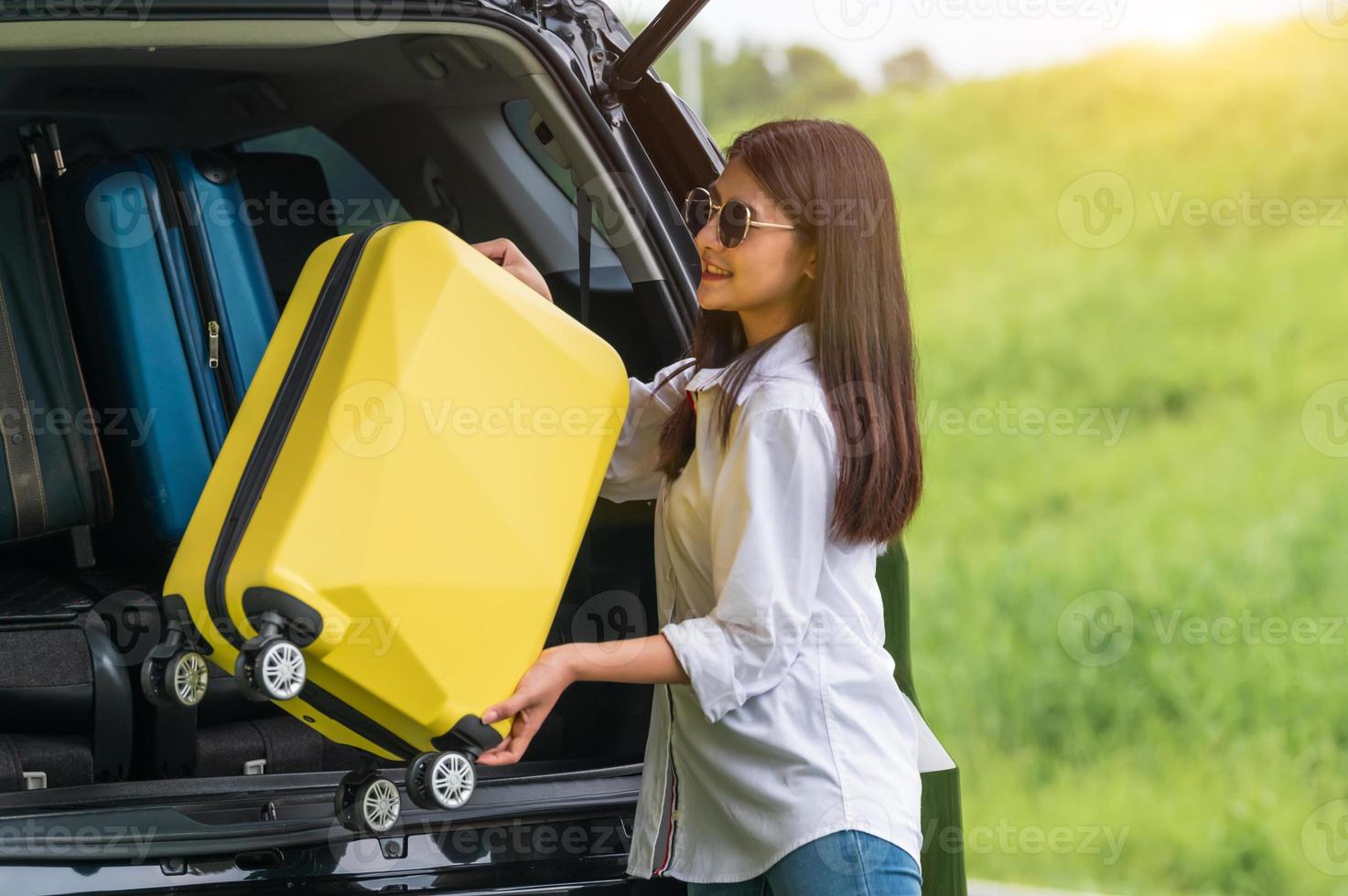 asiatische Frau, die während der Reise gelben Koffer in ein SUV-Auto hebt foto