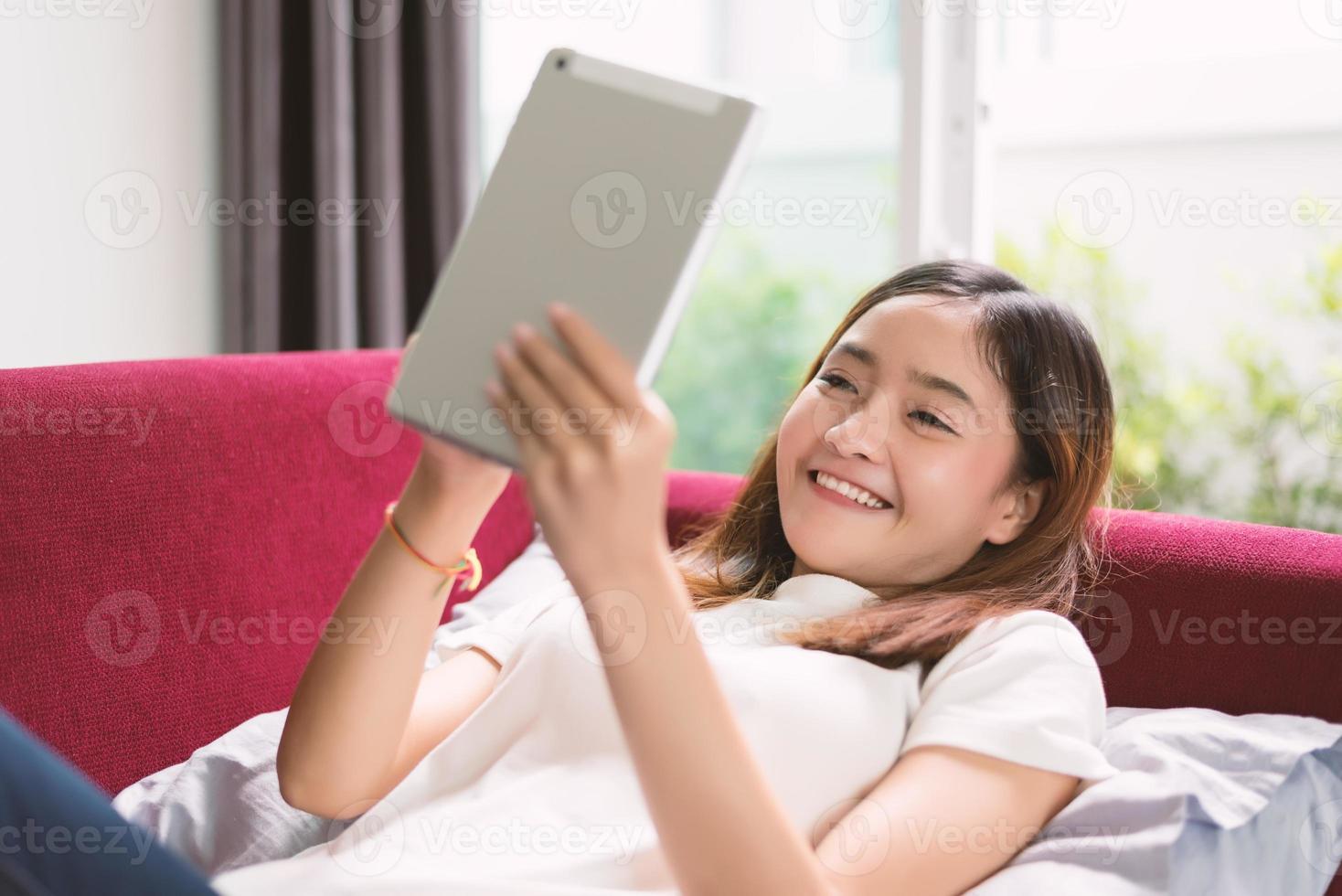 Frau entspannt sich zu Hause mit Tablet auf rotem Sofa foto