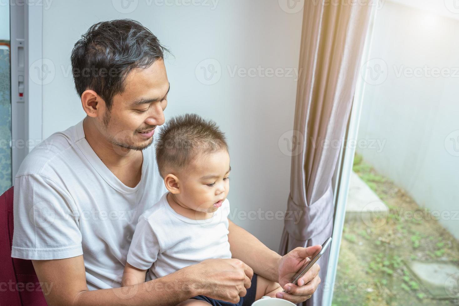 asiatischer vater und sohn, die zusammen zu hause telefon benutzen foto