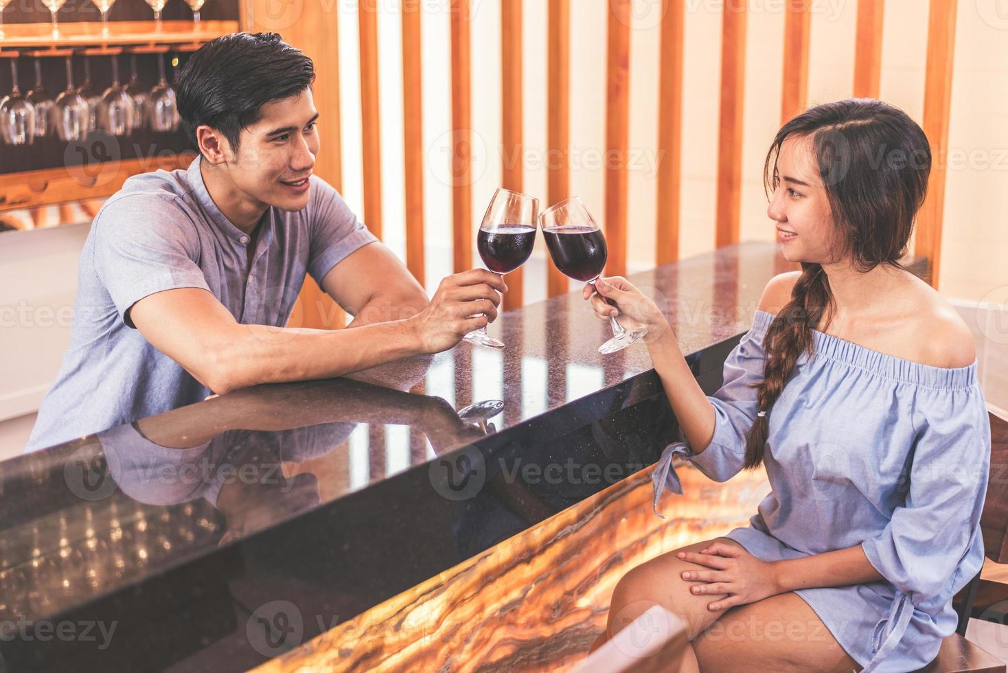 asiatische junge Paare, die an der heimischen Bar Weingläser anstoßen foto