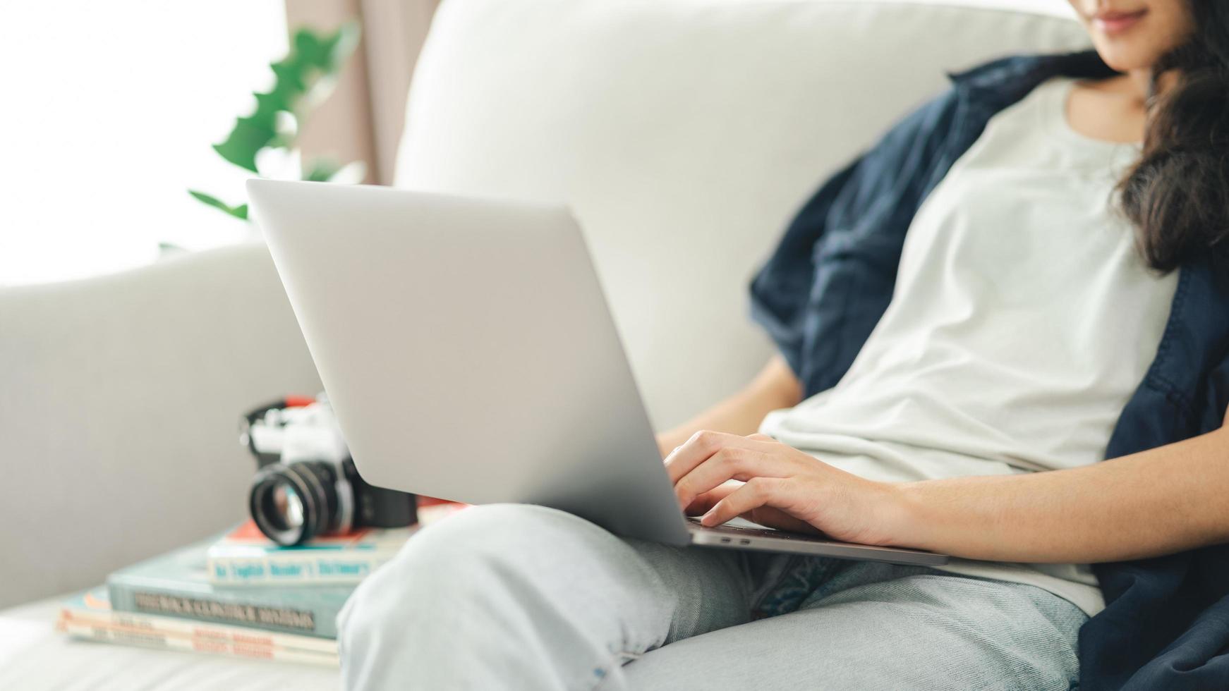 Fotograf sitzt auf der Couch, benutzt den Laptop für die Arbeit mit der Filmkamera foto