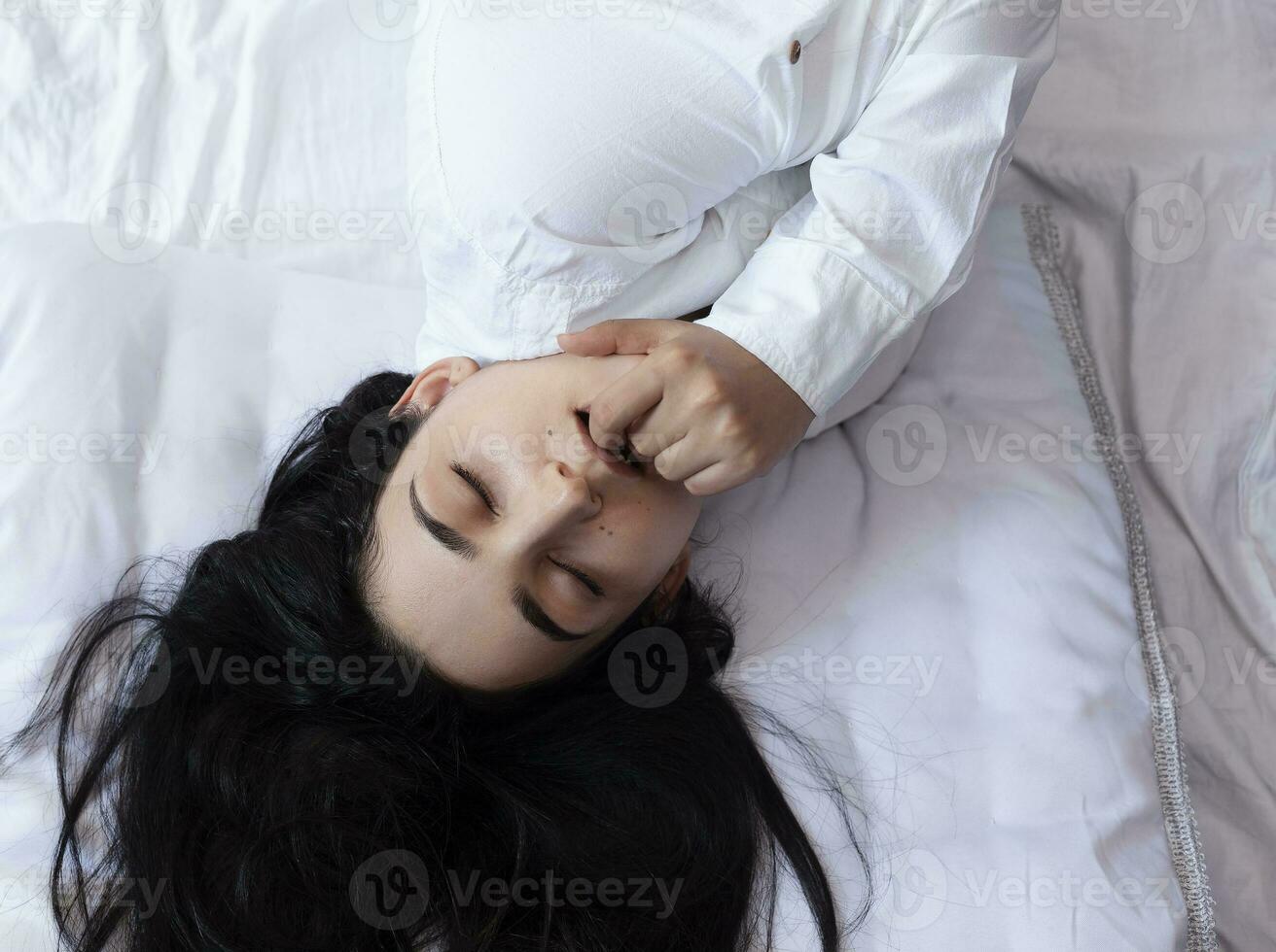 schön Frau Lügen im Bett. sexy schwarz behaart Dame posieren mit ihr Finger im Mund. weiblich genießen, beißen Finger. Gefühl Glücklich, Erholung, Befriedigung und Vergnügen. foto