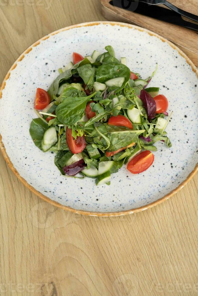 frisch Salat mit Rucola, Kirsche Tomaten, Gurken im ein Teller auf ein Farbe Hintergrund foto